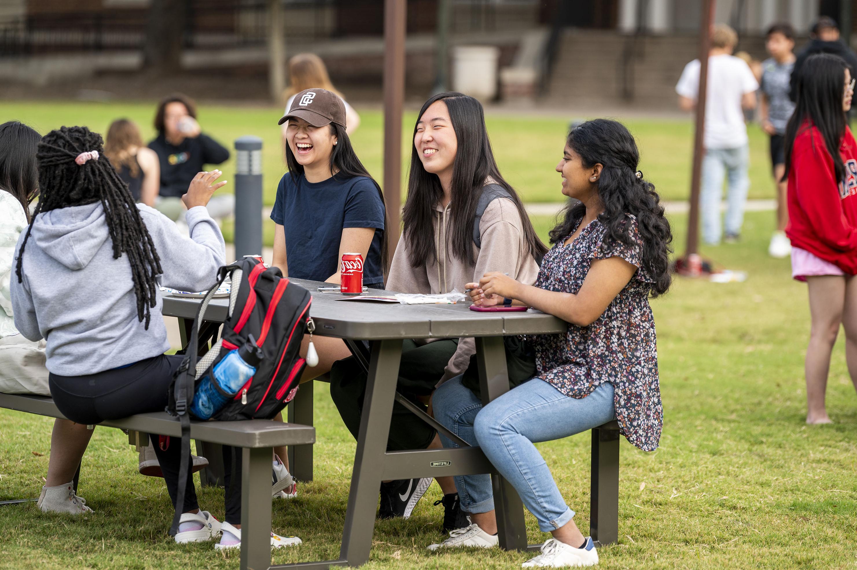 People laughing 和 sitting at a picnic table. 